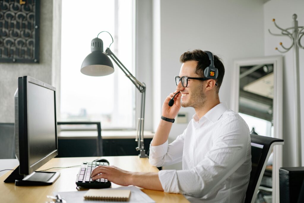 pexels-photo-8867435-8867435 Smiling man wearing headset working at computer in bright office.